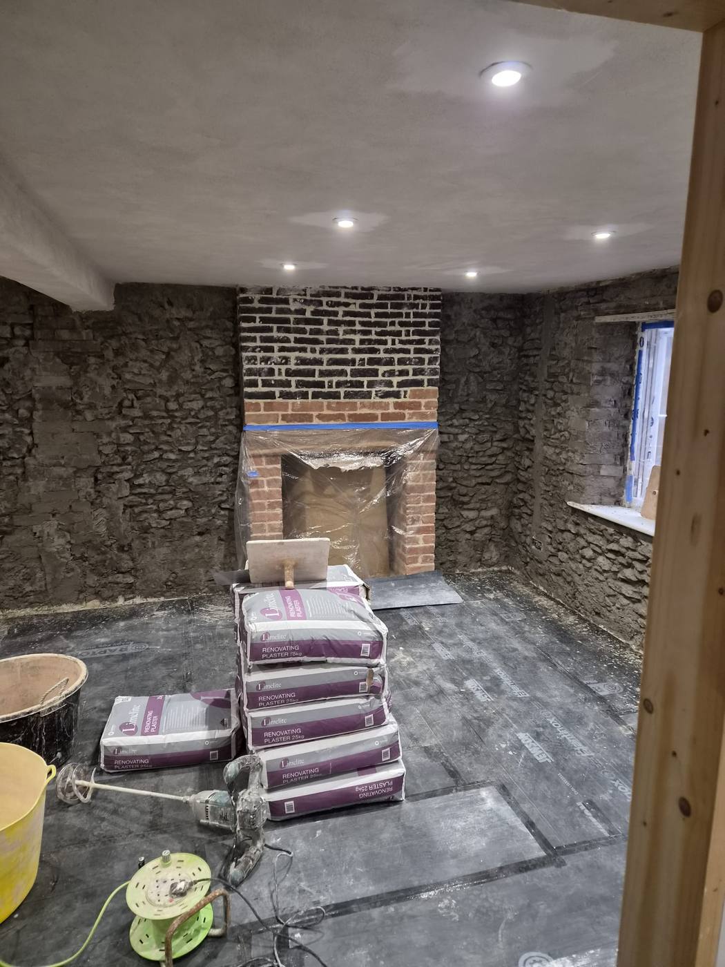 Stone walls prepared with renovating plaster beside a brick fireplace